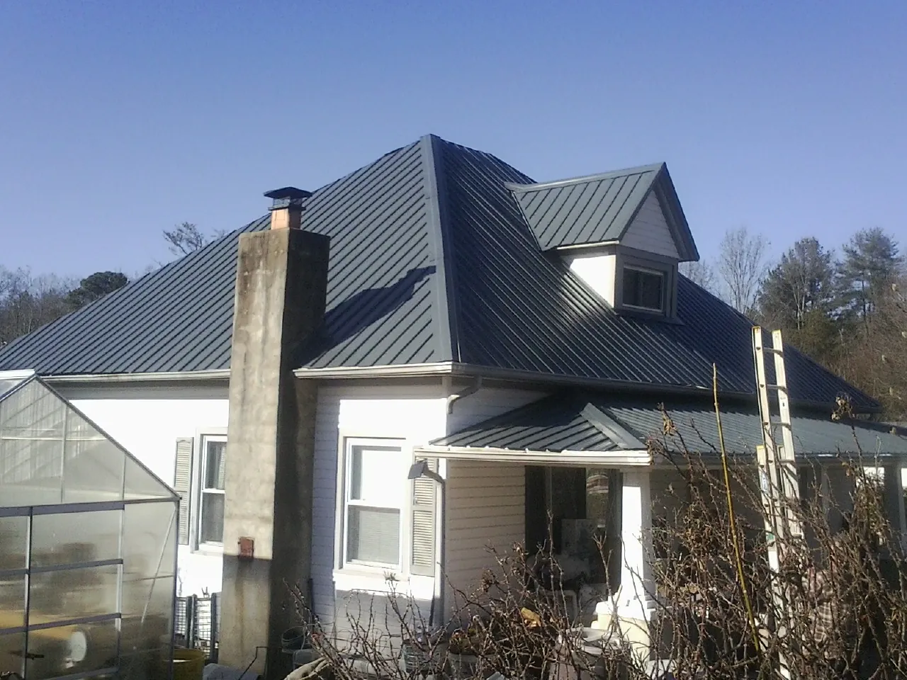 Dark blue standing seam metal roof on a white farmhouse with dormer — Slate & Tile Roof Repair by Roofing Brothers in Scammon