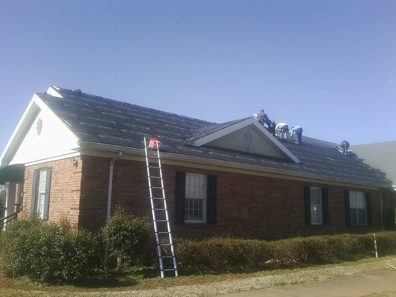 Crew tearing shingles off a brick ranch roof with a ladder set — Metal Roof Repair work by our crew in Scammon