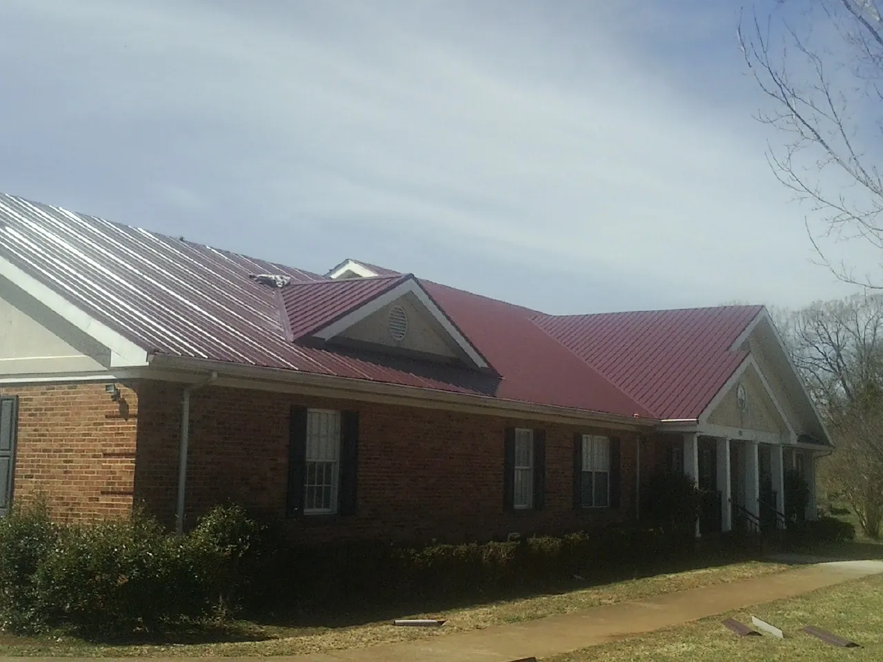Red metal roof with gabled entries on a long brick building, from a Hail Damage Roof Repair job in Scammon