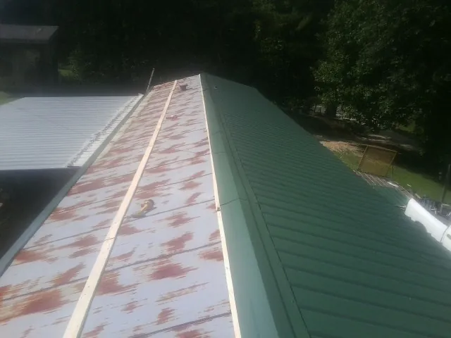 Old rusted panels beside newly installed green metal roofing — Wind Damage Roof Repair by Roofing Brothers in Scammon