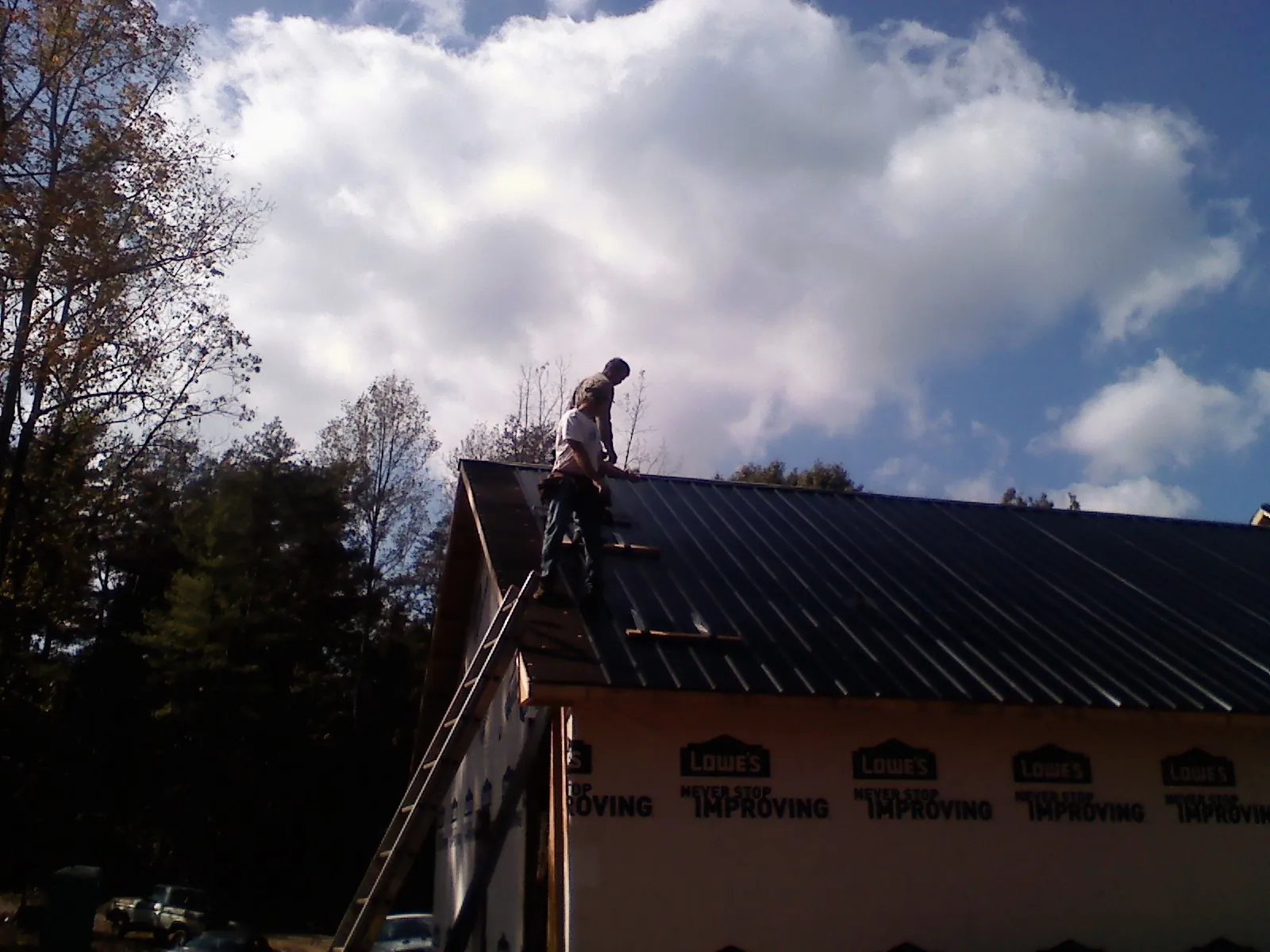Roofer fastening dark metal panels high against a cloudy sky, from a Roof Inspection job in Scammon