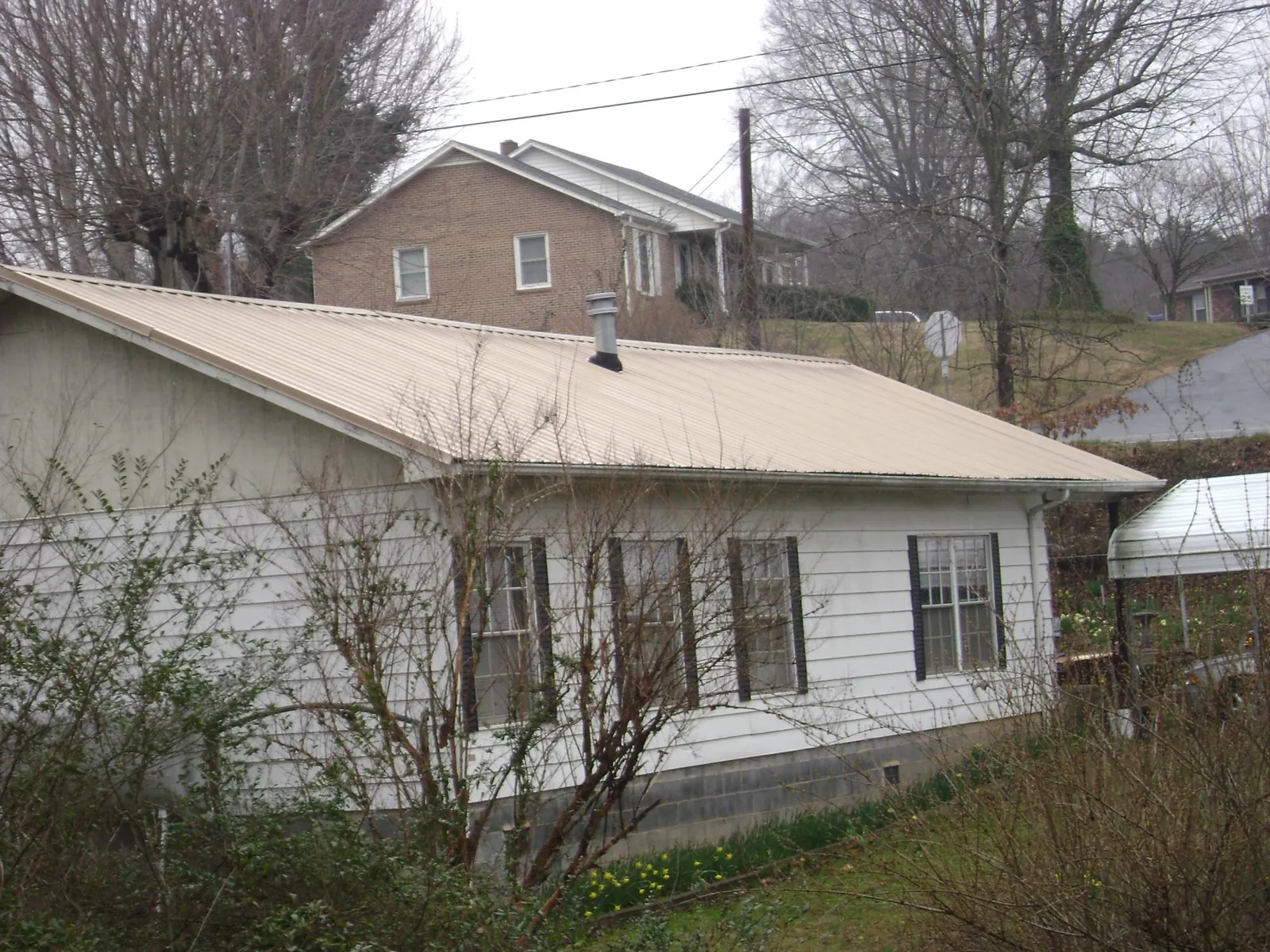 Tan metal roof on a white sided house set into a hillside — Commercial Roofing by Roofing Brothers in Scammon